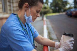 Physician experiencing burnout symptoms sitting outside hospital holding coffee after long shift